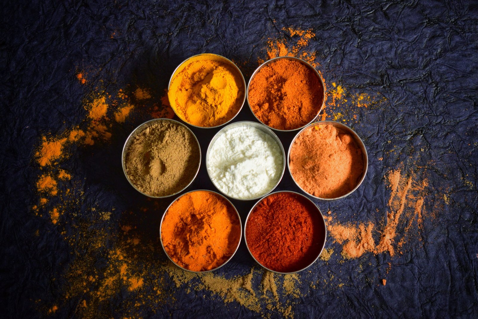 Colorful Indian spices in bowls on a textured dark background for culinary concepts.